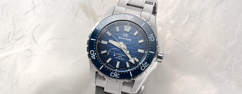 Grand Seiko diver's watch with blue dial and blue bezel shown at an angle on a light marble background.