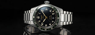 Longines automatic watch with black dial and green bezel on a stainless steel bracelet.