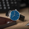 Berlin Automatic 38mm blue dial watch angled on a wooden desk with black leather strap