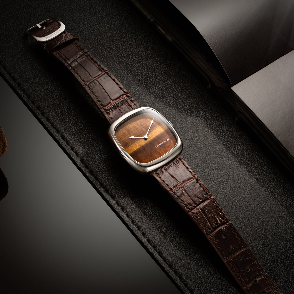 Tiger eye dial watch in steel case with brown alligator pattern leather strap on a black textured surface