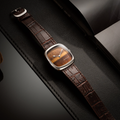 Tiger eye dial watch in steel case with brown alligator pattern leather strap on a black textured surface
