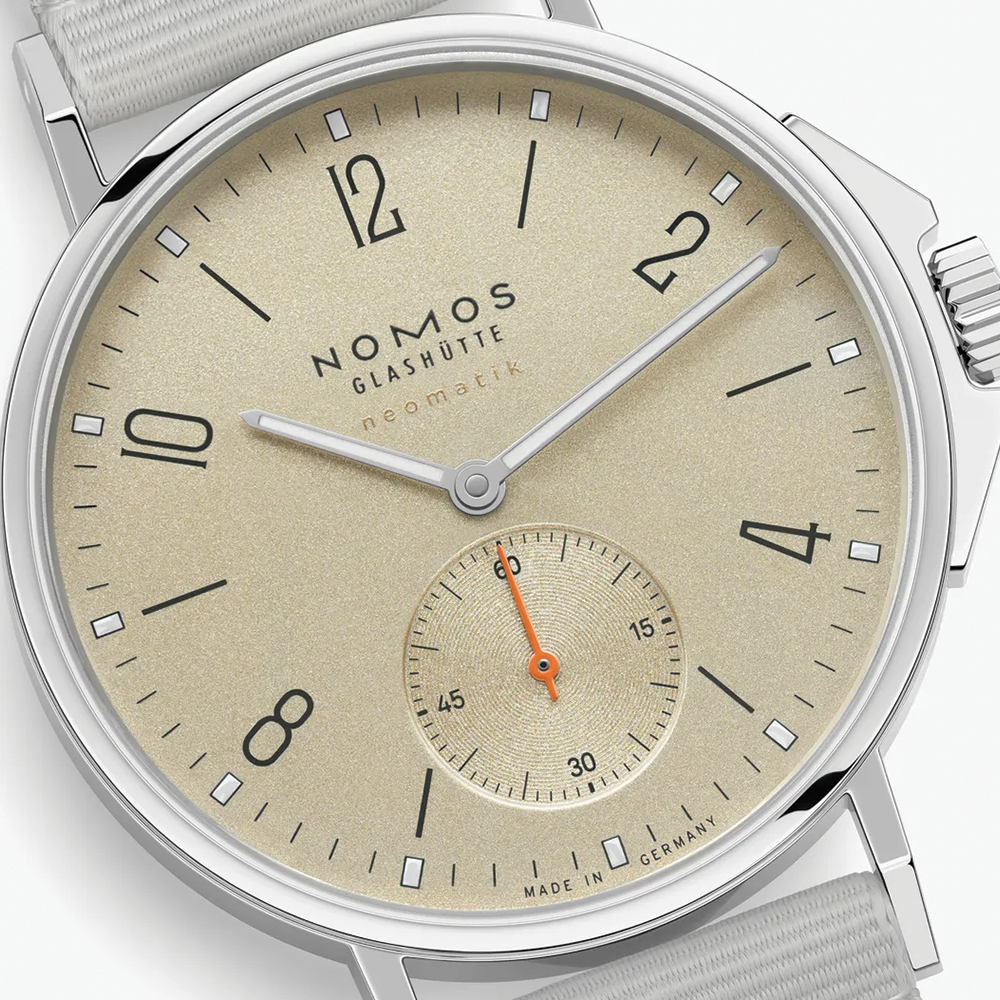 Close-up of beige dial with orange seconds hand from Nomos Ahoi Neomatik Sand on fabric strap