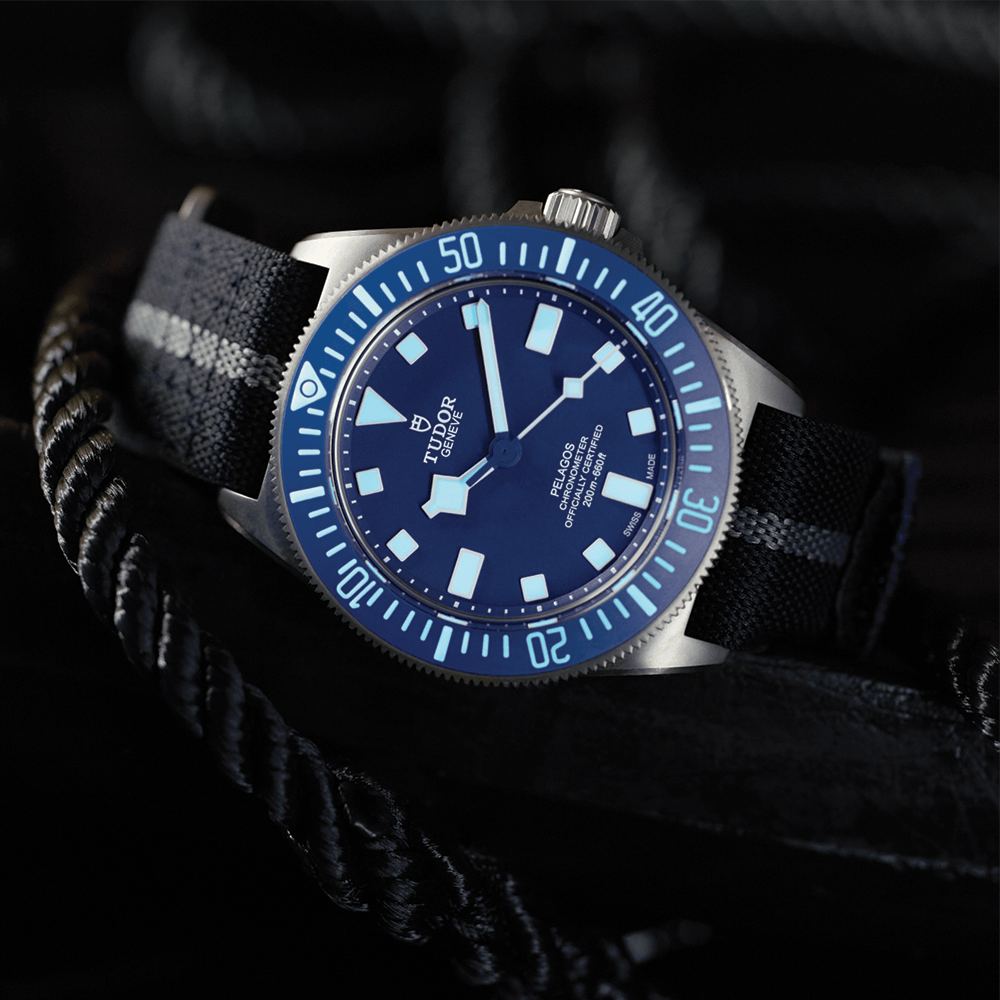 Tudor Pelagos FXD 42mm blue dial dive watch angled on a dark surface with striped fabric strap