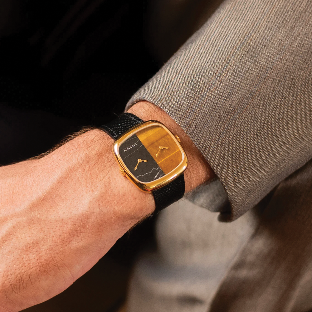 Wrist view of the gold ALD Dual Time watch with tiger eye and marble dial on a black leather strap