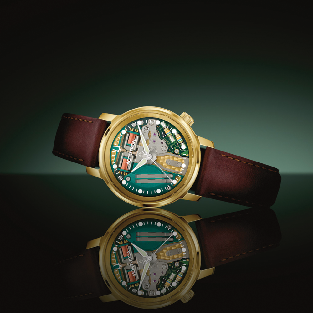 Angle view of a gold-tone Spaceview 314 Limited Edition watch with green dial and brown leather strap, reflected on a glossy surface.