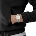 Wrist shot of a Tissot PR 100 chronograph on a stainless steel bracelet with beige mother-of-pearl dial worn with a black jacket