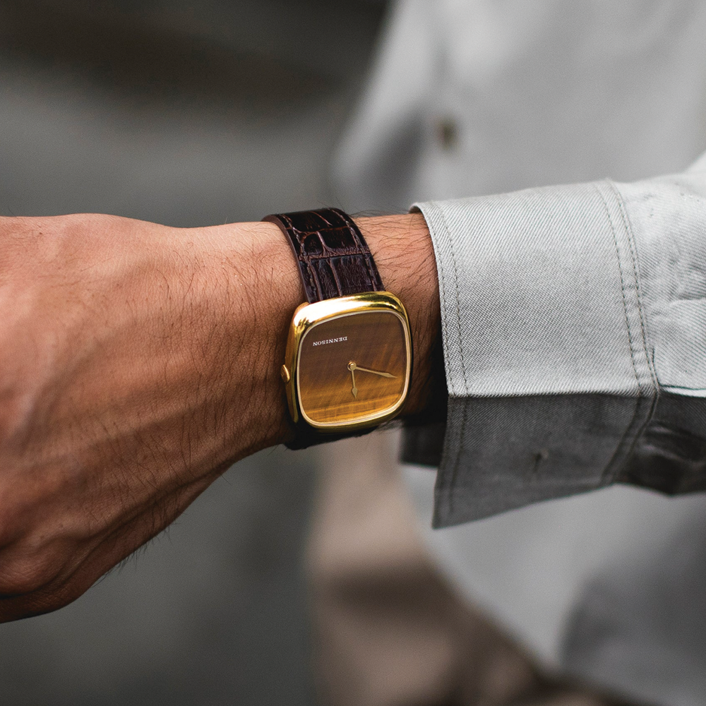 Wrist view of a gold case tiger eye watch on a brown leather strap