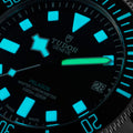 Macro shot of Tudor Pelagos dial with cyan luminous markers and a green luminous minute hand.